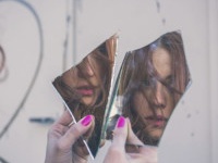 Beautiful redhead girl with long hair and blue eyes looking at herself in a broken mirror