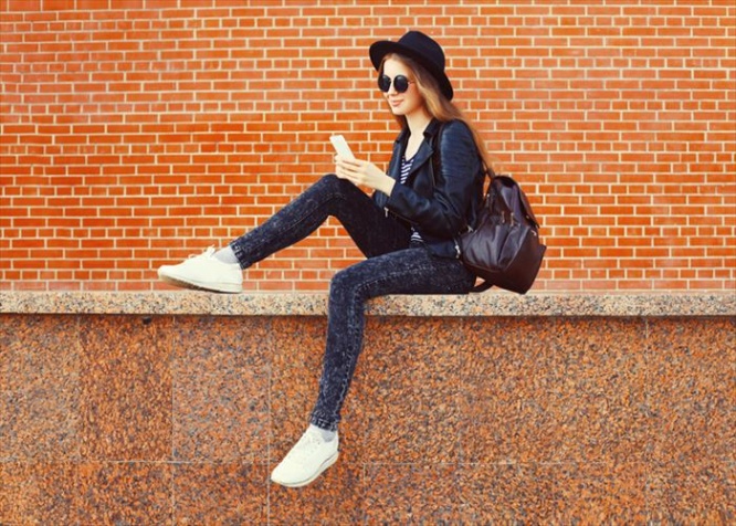 Fashion pretty woman using smartphone in rock black style over bricks textured background