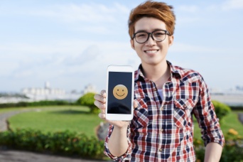 Vietnamese guy showing smiling emoji on the screen of his smartphone