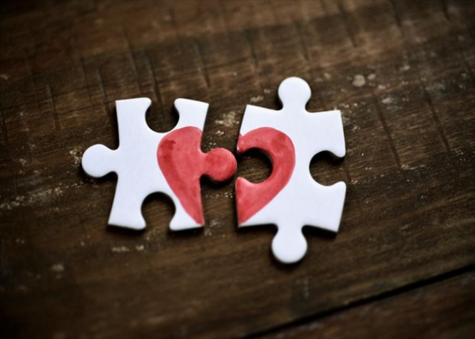 closeup of two separated pieces of a puzzle which together form a heart on a rustic wooden surface, depicting the idea of rupture or cooperation