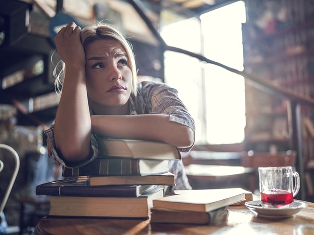 Worried student thinking of her upcoming exams in a library.