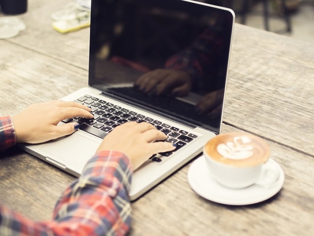 woman typing on a laptop with cup of coffee