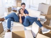 Moving, repairs, new flat. Couple in love hugging lying down and looking at the camera to move and wife hugging her husband while man and woman lying on the sofa among the boxes in an empty apartment