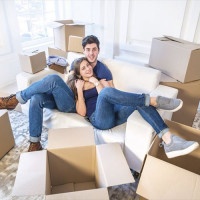 Moving, repairs, new flat. Couple in love hugging lying down and looking at the camera to move and wife hugging her husband while man and woman lying on the sofa among the boxes in an empty apartment